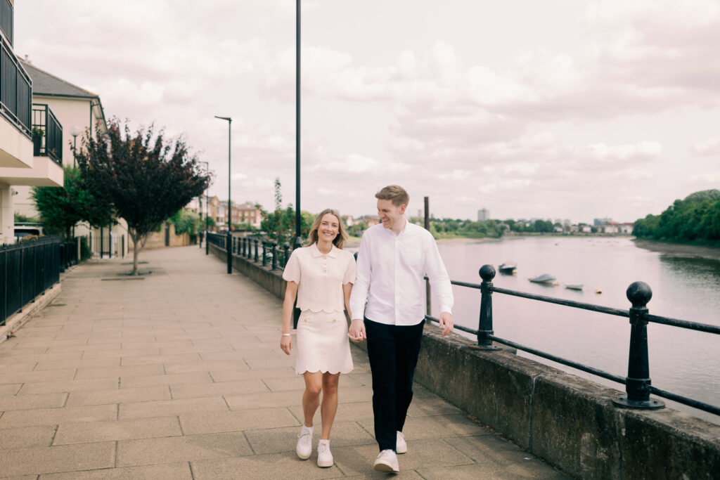 Romantic couple walking hand in hand along River Thames Chiswick London engagement